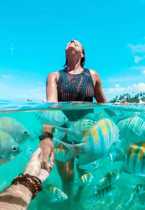 Mulher olhando para o sol em um lindo mar transparente e com peixes coloridos