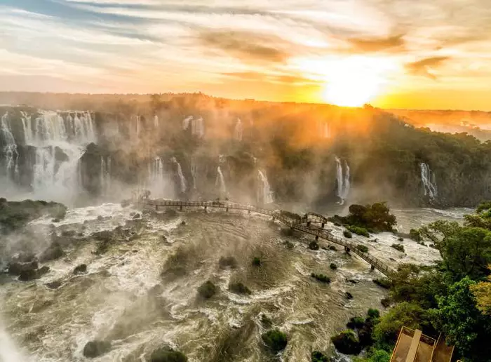 Paisagem inspiradora das Cataratas do Iguaçu, quedas d'água vistas de longe e céu ensolarado.