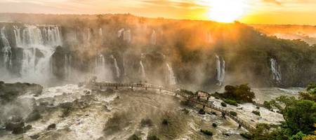 Paisagem inspiradora das Cataratas do Iguaçu, quedas d'água vistas de longe e céu ensolarado.