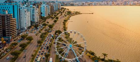 Vista aérea da cidade de Florianópolis à beira-mar, pôr do sol e roda gigante ao fundo.