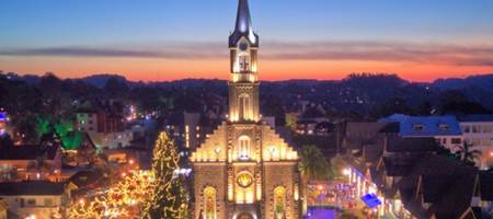 Foto panorâmica da Paróquia de São Pedro no centro de Gramado, ruas em volta todas iluminadas de noite.
