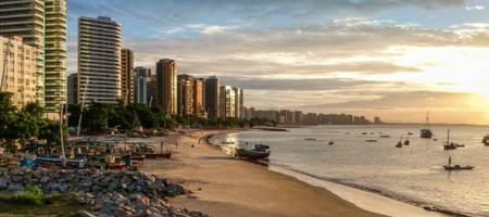 Lindo final de tarde na Praia do Iracema, em Fortaleza, com o mar refletindo a luz do sol e prédios por toda a orla.