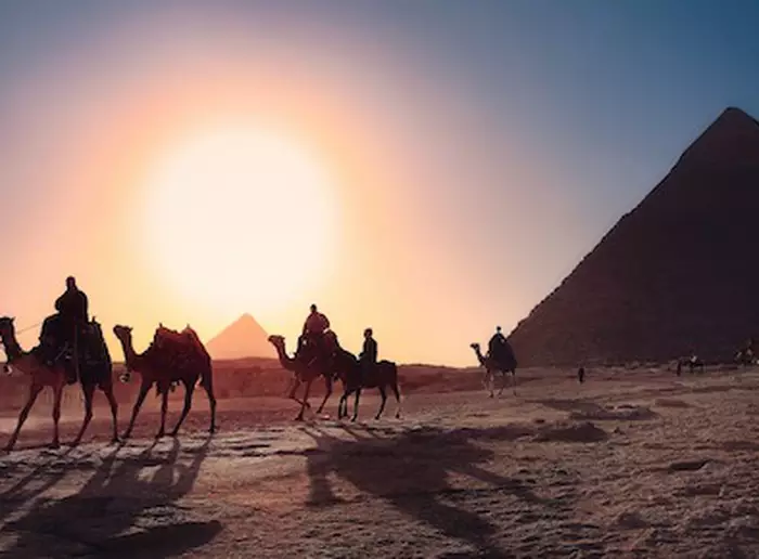 Por do Sol no Egito, com pessoas andando em camelos e pirâmides ao fundo