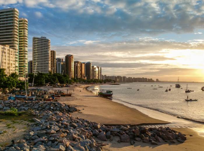 Lindo final de tarde na Praia do Iracema, em Fortaleza, com o mar refletindo a luz do sol e prédios por toda a orla.
