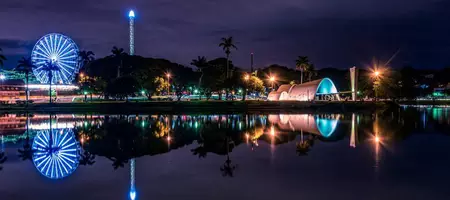 Linda vista noturna do Conjunto Arquitetônico da Pampulha, com a roda gigante iluminada refletindo na lagoa da Pampulha.