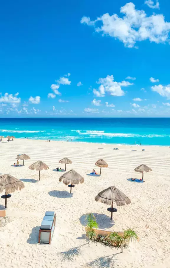 Fotografia de uma praia paradisíaca em Cancún, com um guarda sol de palha proporcionando sombra sobre a areia fina. O refúgio perfeito para relaxar e desfrutar da beleza natural.