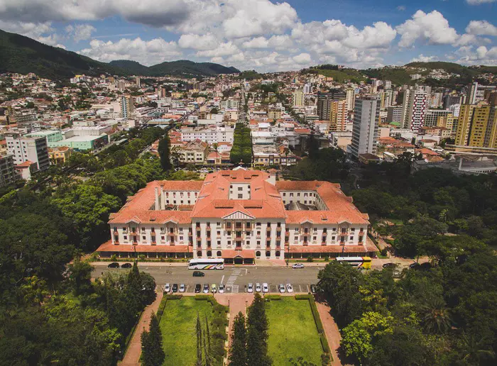 Vista aérea de Poços de Caldas, destacando o histórico Palace Hotel cercado por jardins verdes e o vibrante cenário urbano ao redor.